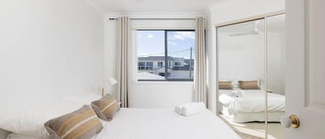 A bedroom with a bed, a window, a ceiling fan, and a sliding glass door.