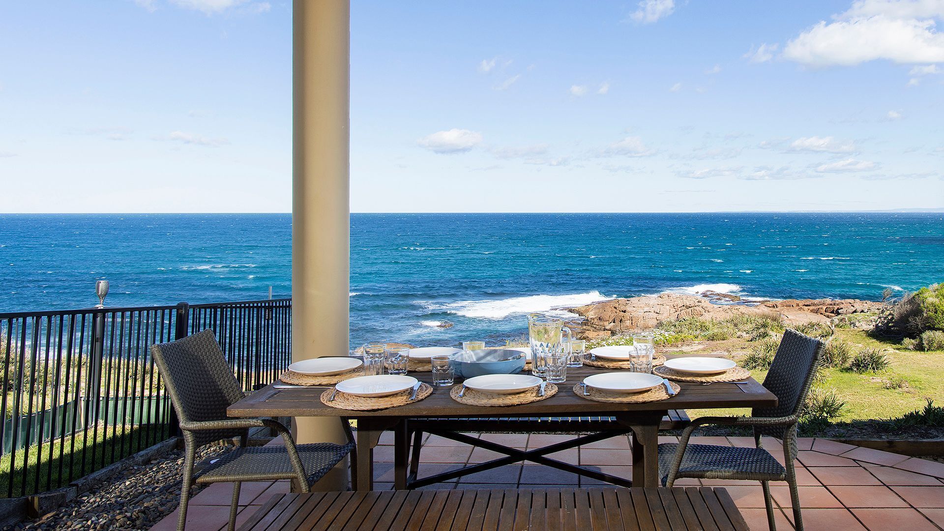 An outdoor dining area with a table set for four, overlooking the ocean.