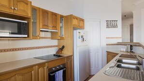 Una cocina con gabinetes de madera, microondas, refrigerador y pileta.