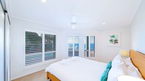 A bedroom with a bed, a ceiling fan, and large windows with blinds.
