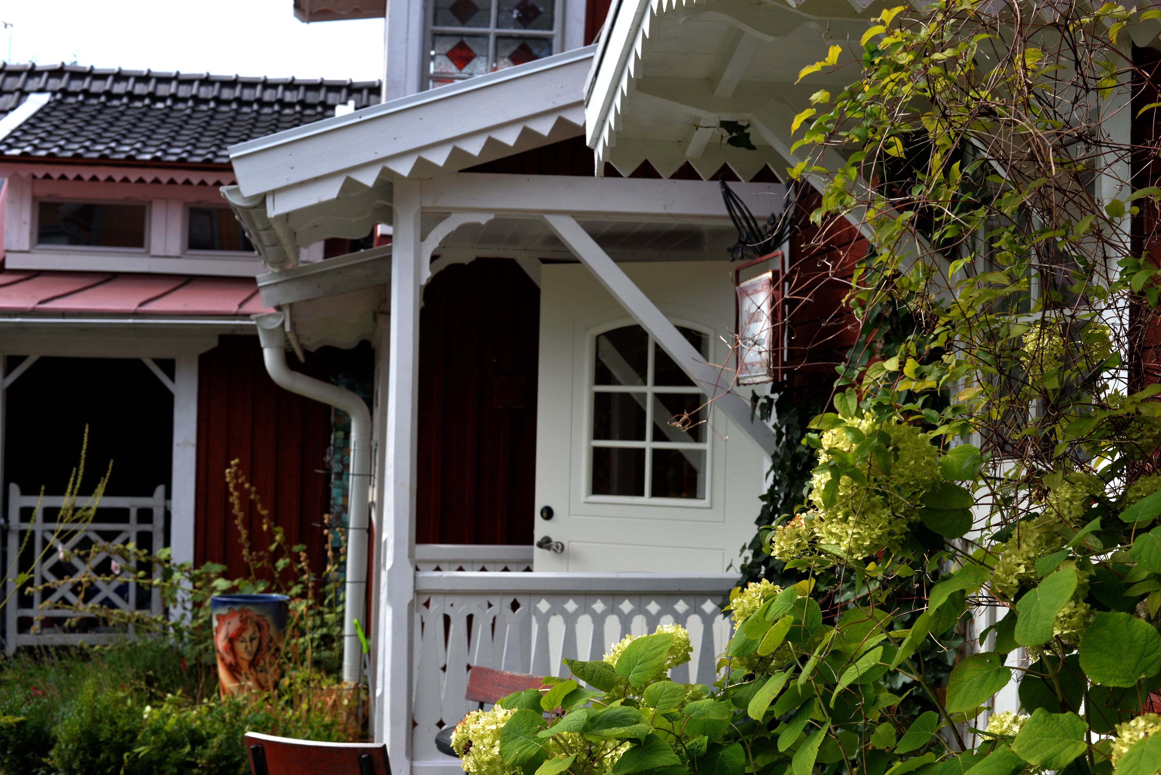 Ett traditionellt hus med en vit veranda, en röd dörr och ett fönster.