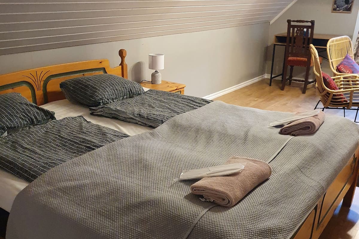 Un dormitorio con una cama de madera, una mesita de noche con una lámpara y una silla.