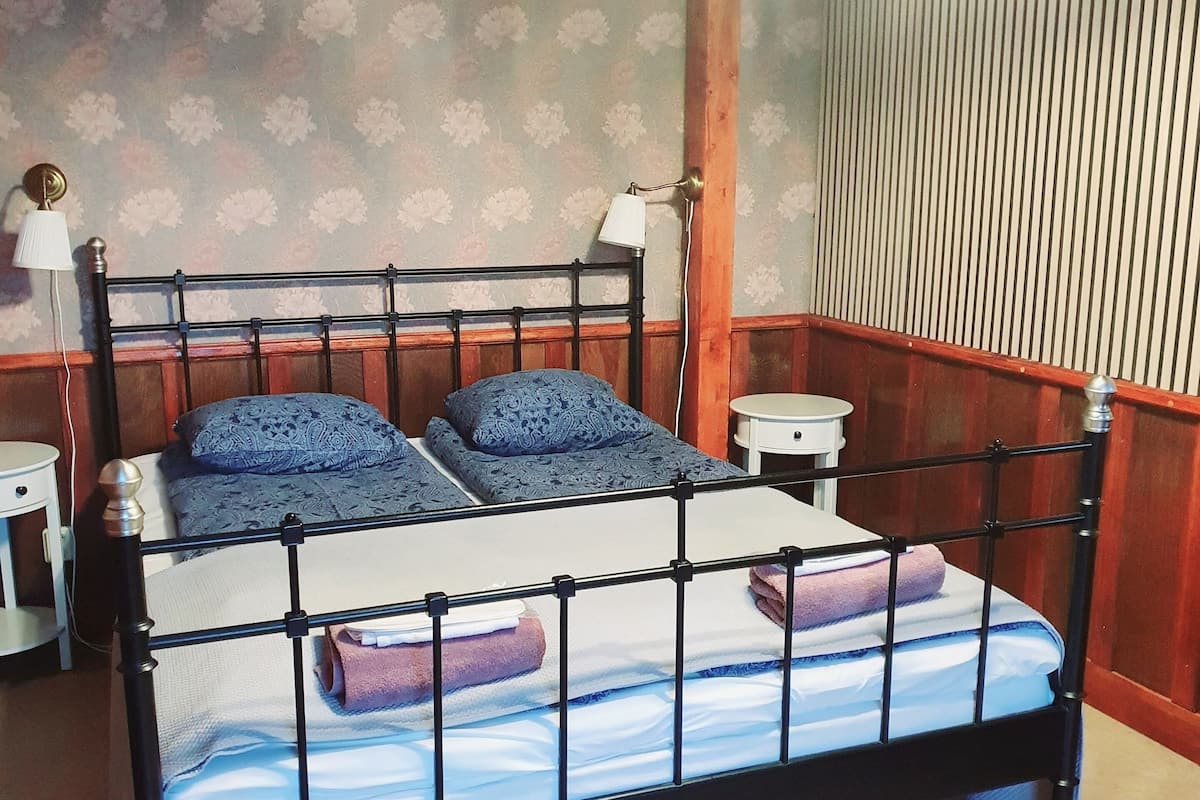 Un dormitorio con estructura de cama metálica, dos mesitas de noche, una lámpara de pared y un ventilador de techo.