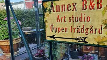 Un hivernacle amb un cartell que diu "Annex B&B Art studio Öppen trädgård" i plantes en testos a l'interior.