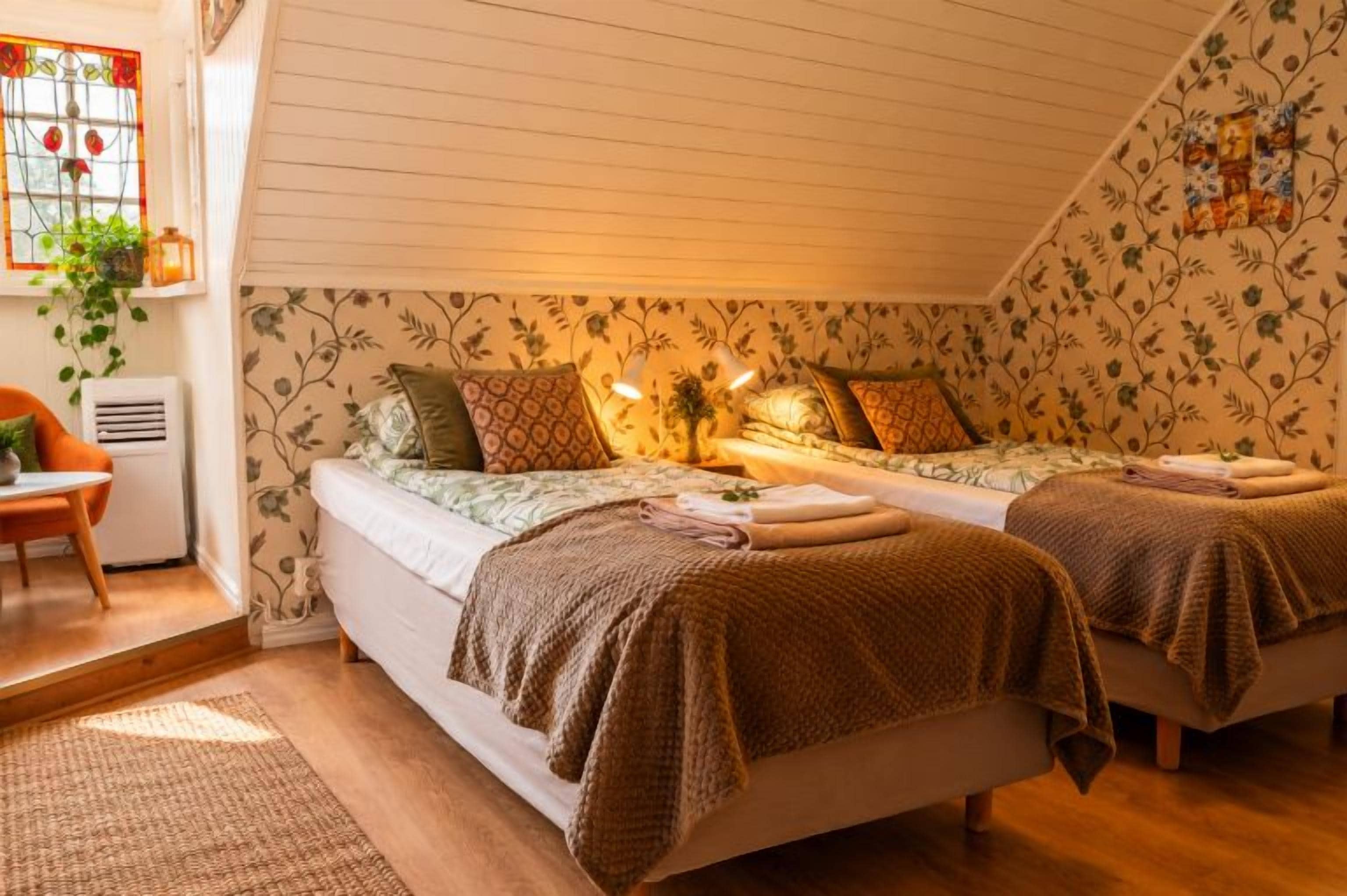 A cozy bedroom with two beds, a chair, and a window with a plant.