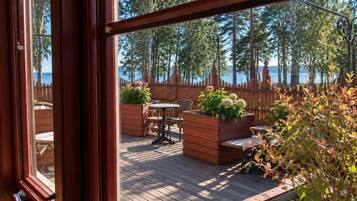 Terraza de madera con mobiliario exterior y jardineras, con vistas a un cuerpo de agua y árboles.