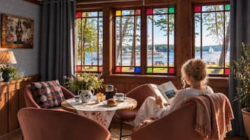 Une pièce avec vue sur un lac, une table avec une théière et une personne qui lit un livre.