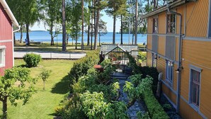 A garden with a stone pathway, a red building, and a yellow building with a window overlooking a body of water.