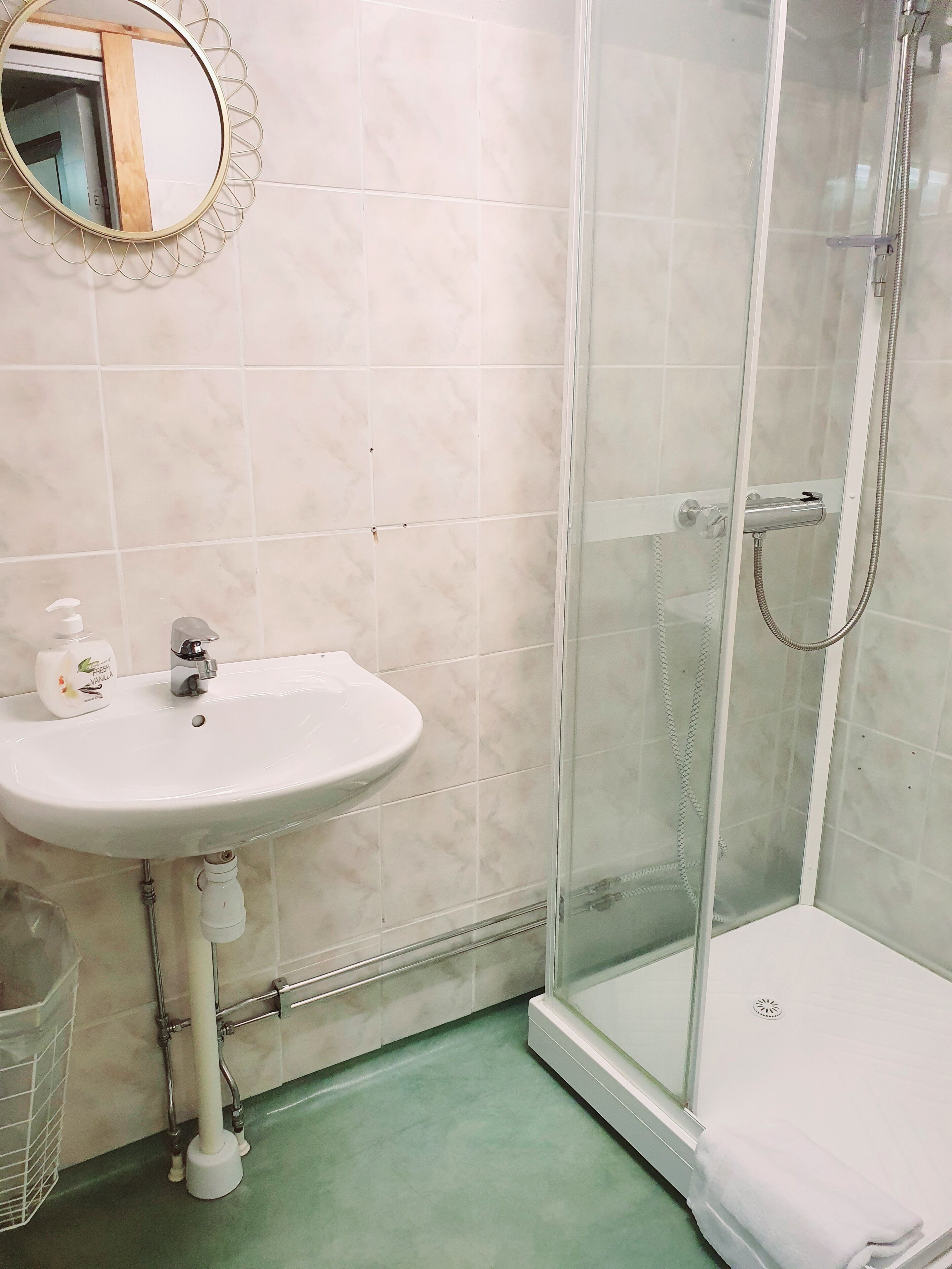 Un baño con lavamanos blanco, cabina de ducha de vidrio y espejo con marco decorativo.