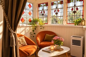 A room with two orange chairs, a white table with a vase and candle, and a window with stained glass. - Nymans Bed & Breakfast (Karlsborg)