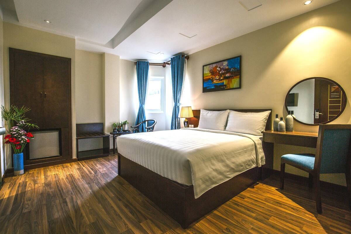 A hotel room with a large bed, a desk, a chair, a mirror, and a window with curtains.