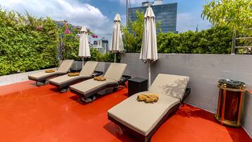 A rooftop lounge area with sun loungers, umbrellas, and a red floor.
