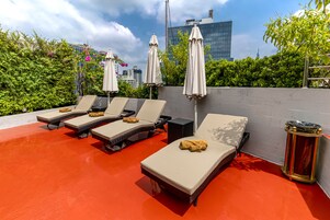 A rooftop lounge area with sun loungers, umbrellas, and a red floor.