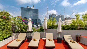A rooftop lounge area with six sunbeds, each with a towel, and two umbrellas. - Roseland Sweet Hotel (Ho Chi Minh City)