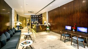 A hotel lobby with a reception desk, a sofa, two chairs, a small table, and two laptops on a desk. - Roseland Sweet Hotel (Ho Chi Minh City)