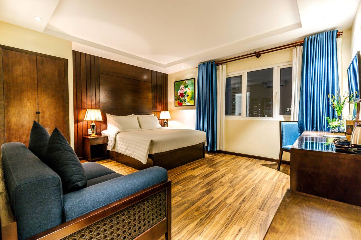 A hotel room with a bed, a sofa, a desk, and a window with curtains.