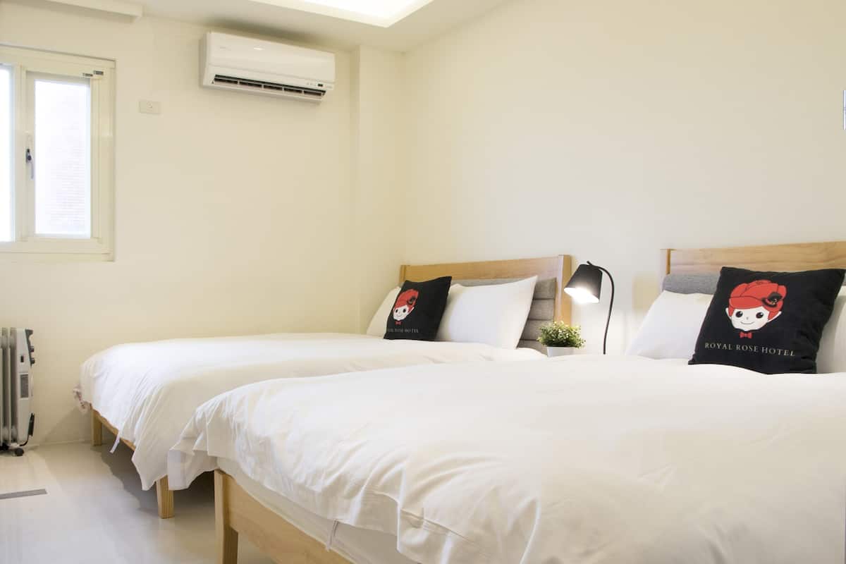 Habitación de hotel con dos camas, ropa de cama blanca, una planta pequeña en maceta y un aire acondicionado de pared.