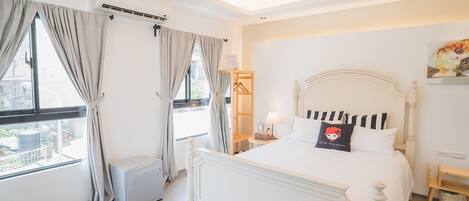 A hotel room with a large bed, a bedside table with a lamp, a window with curtains, and an air conditioning unit.