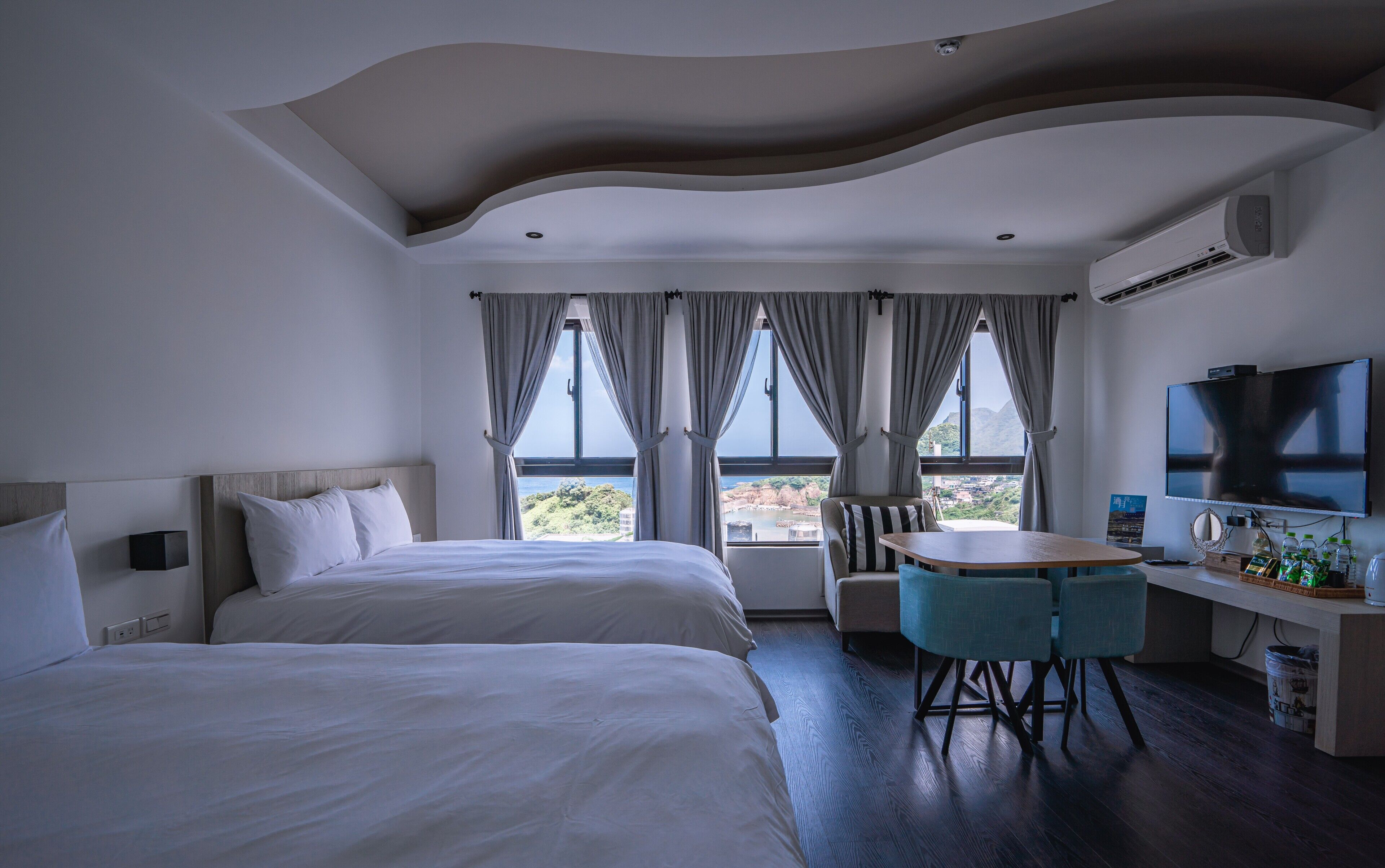 Habitación de hotel con dos camas, una mesa de comedor con sillas, televisión y vistas al exterior.