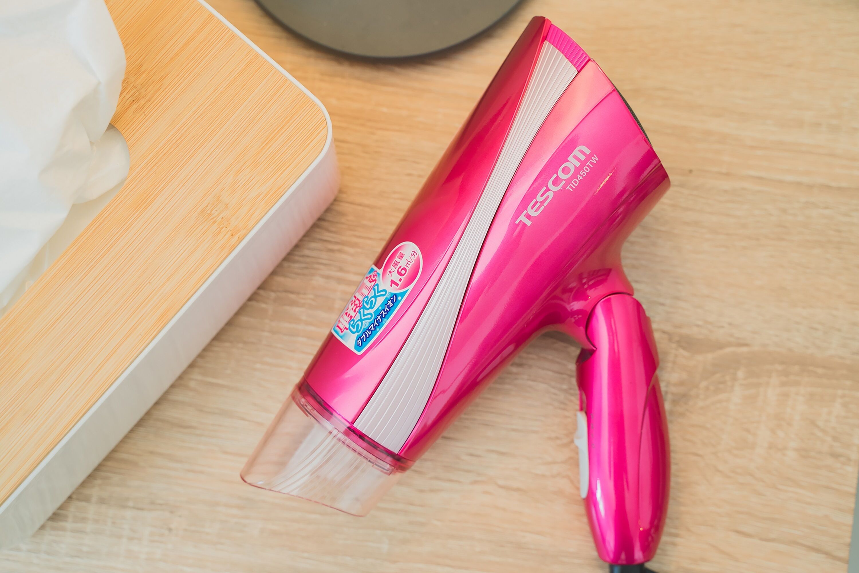 A pink hairdryer with a transparent nozzle on a wooden surface.