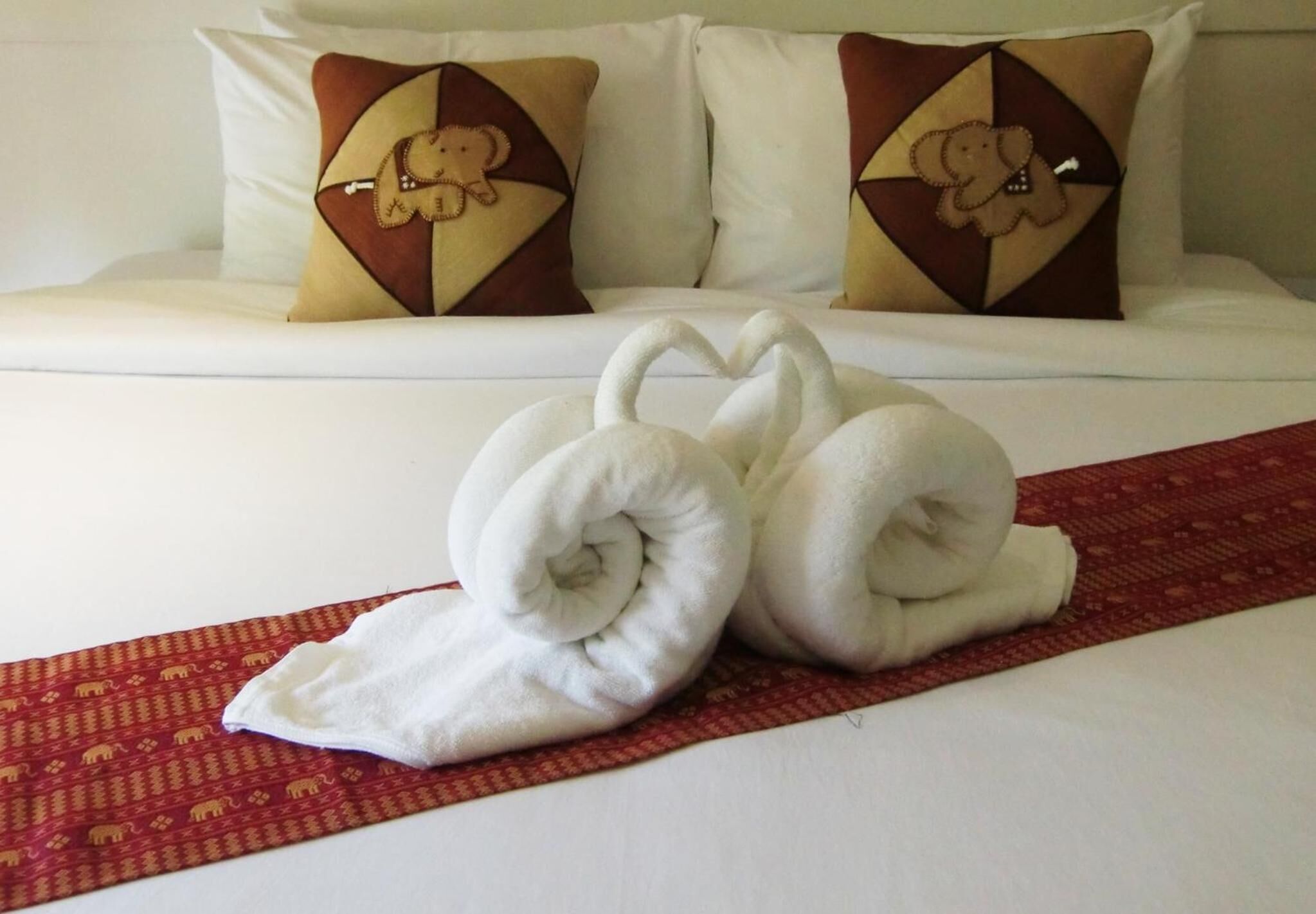 A neatly made bed with two pillows featuring a geometric pattern and a red decorative strip.