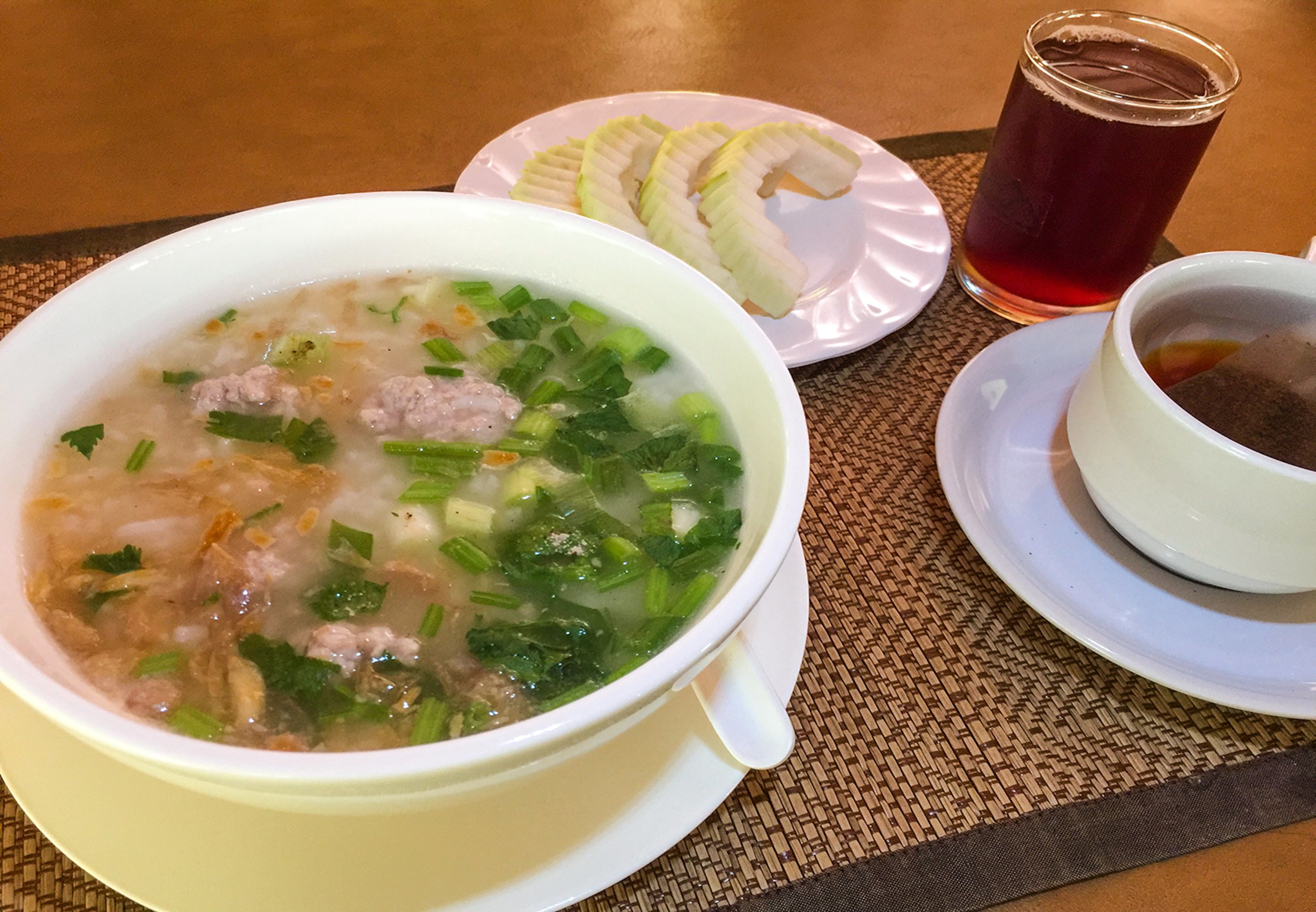 Un tazón de sopa con carne y verduras, un plato de plátanos en rodajas, y un vaso de té sobre una mesa.