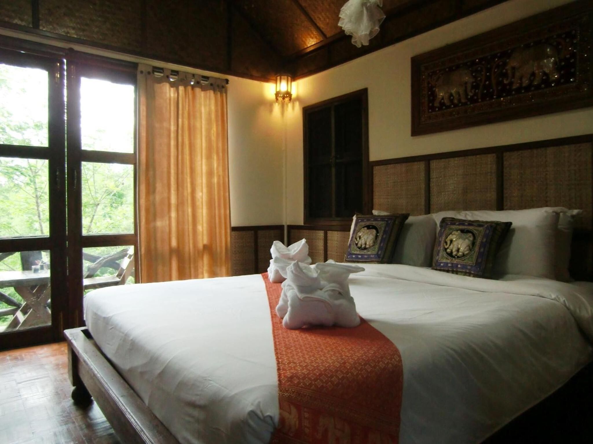 A hotel room with a large bed, a window with curtains, a wall-mounted light, and a framed picture above the bed.