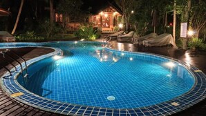 Ein Schwimmbecken mit einer gefliesten Kante, umgeben von Liegestühlen und einem überdachten Bereich.
