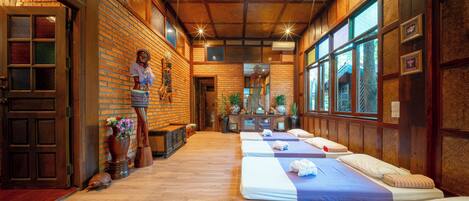 A room with wooden floors, brick walls, and a long row of beds with blue and white bedding.