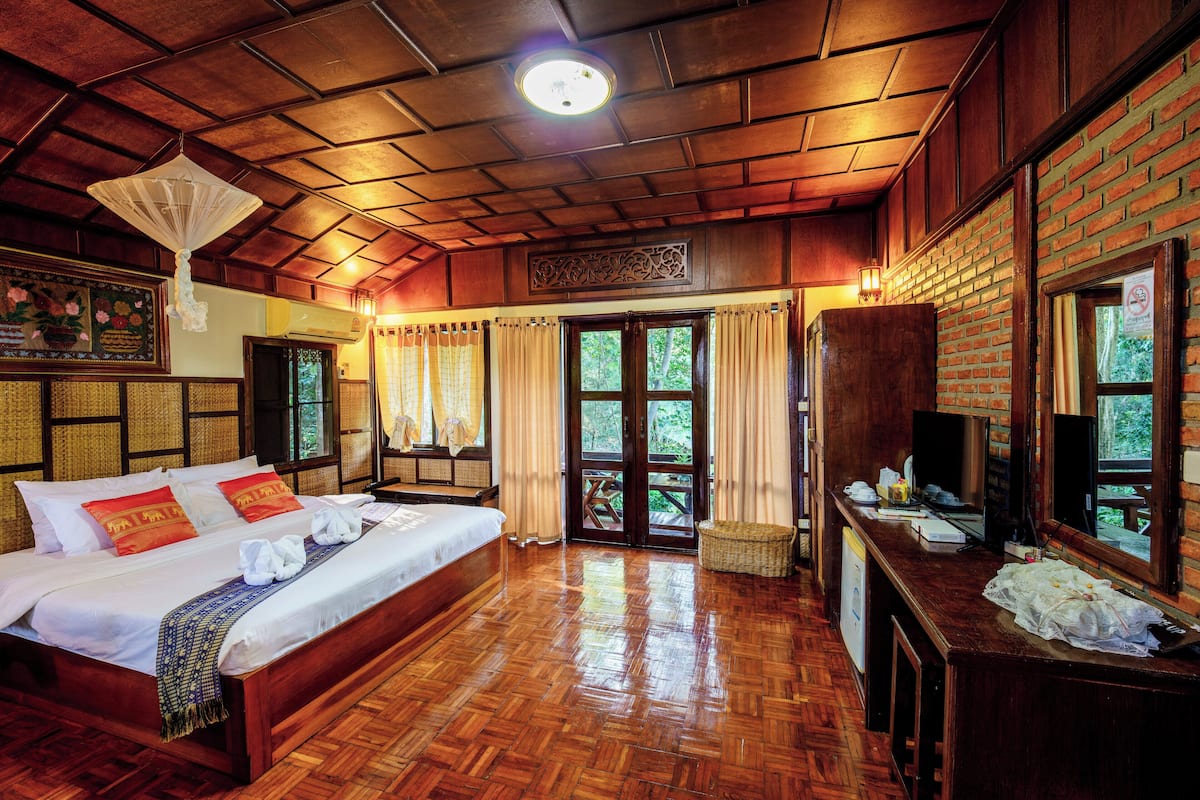 A wooden-floored bedroom with a bed, curtains, and a television.