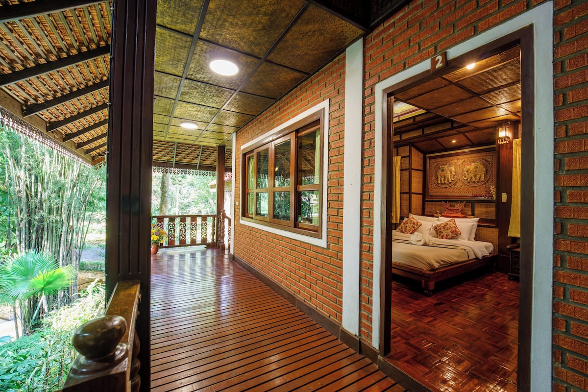A wooden deck leading to a room with a bed, a large window, and a brick wall.
