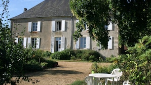 A two-story house with a gravel driveway and a garden with a table and chairs. - Chambres d'hotes du Jay (La Guerche-sur-l'Aubois)