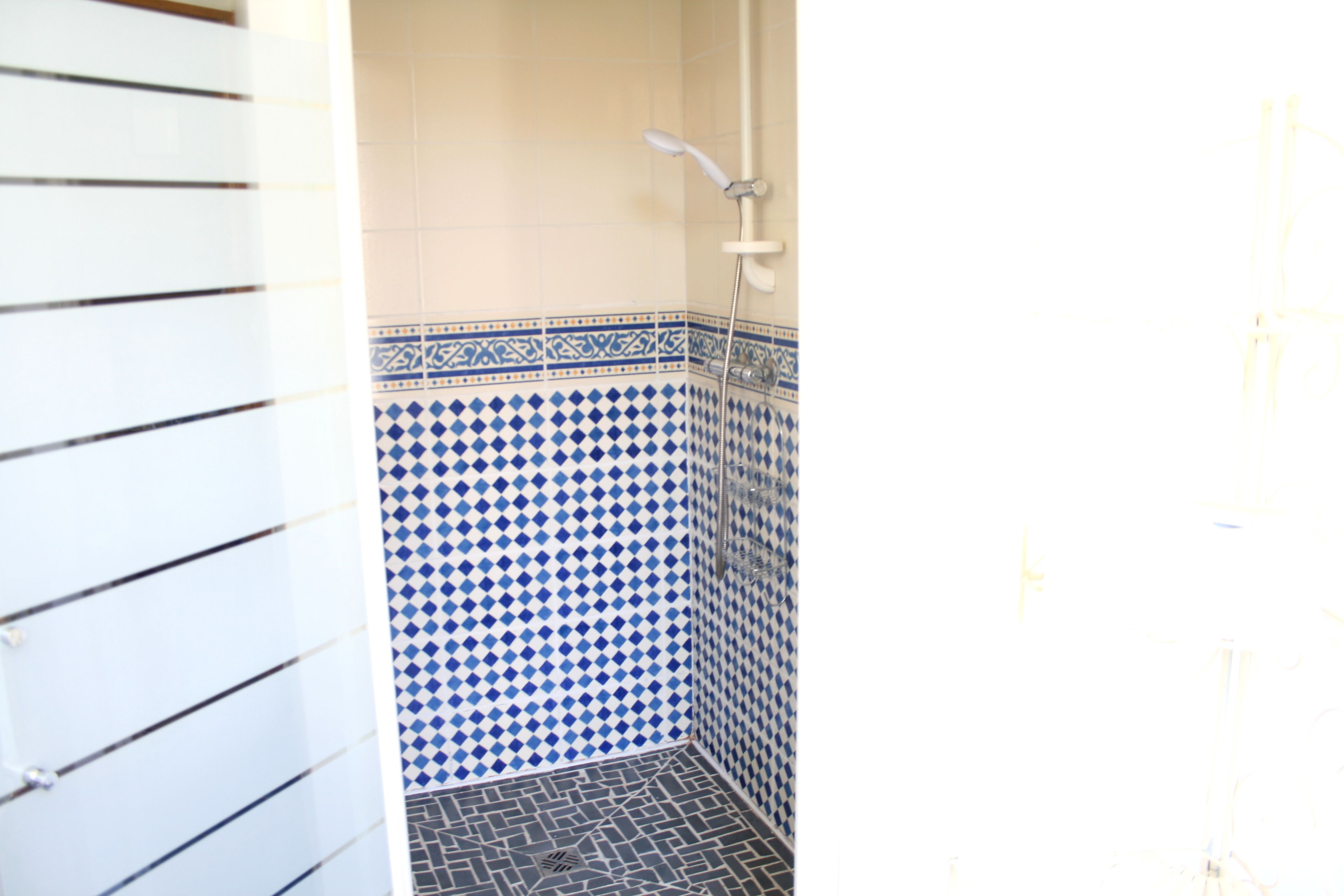 Un baño con azulejos blancos y azules con diseño, una ducha y suelo de baldosas.