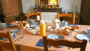 A dining table set with plates, bowls, and a pitcher of orange juice, surrounded by wooden chairs. - Chambres d'hotes du Jay (La Guerche-sur-l'Aubois)