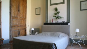 A bedroom with a large bed, a wooden wardrobe, a small table with a lamp, and a plant on a shelf. - Chambres d'hotes du Jay (La Guerche-sur-l'Aubois)