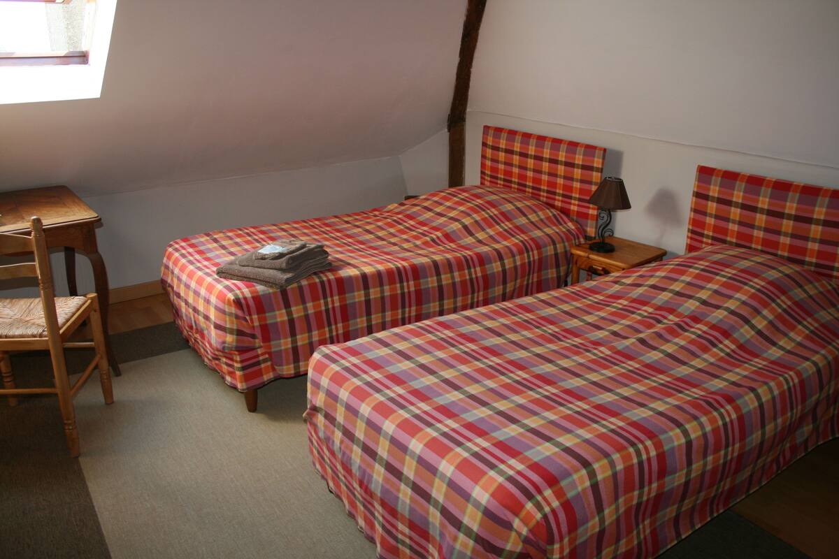 A small, cozy room with two beds, a wooden desk, and a chair.