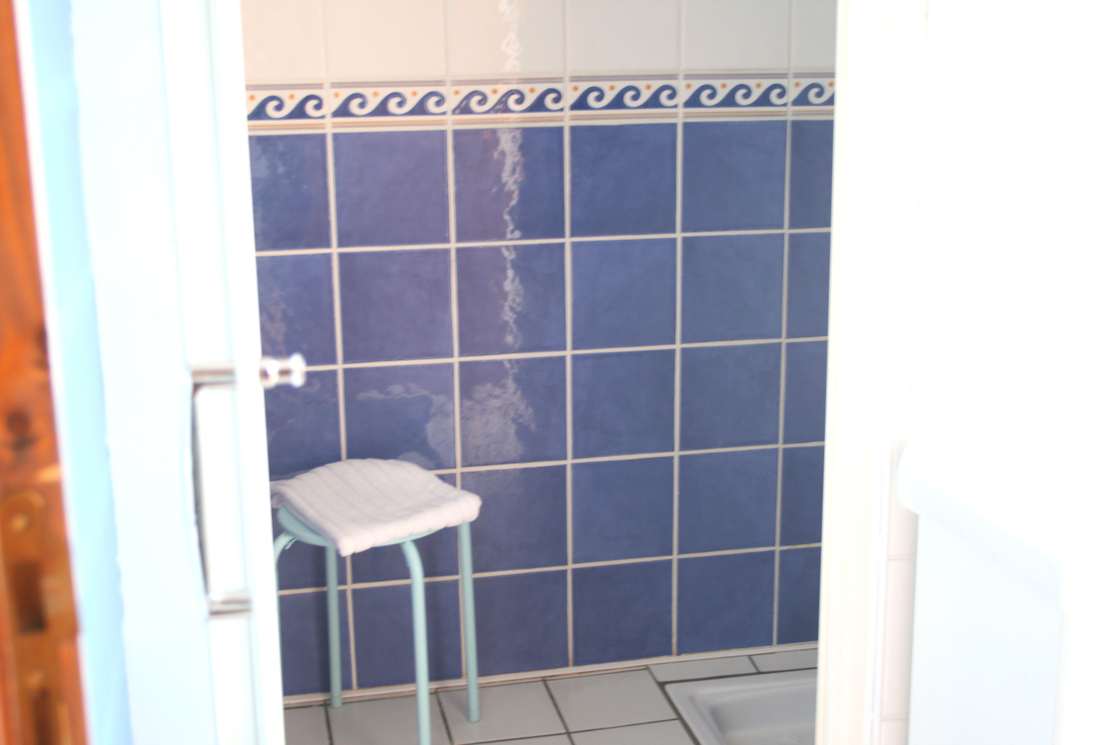 A bathroom with blue tiled walls, a white toilet, and a blue stool.