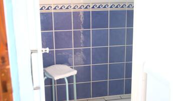 A bathroom with blue tiled walls, a white toilet, and a blue stool.