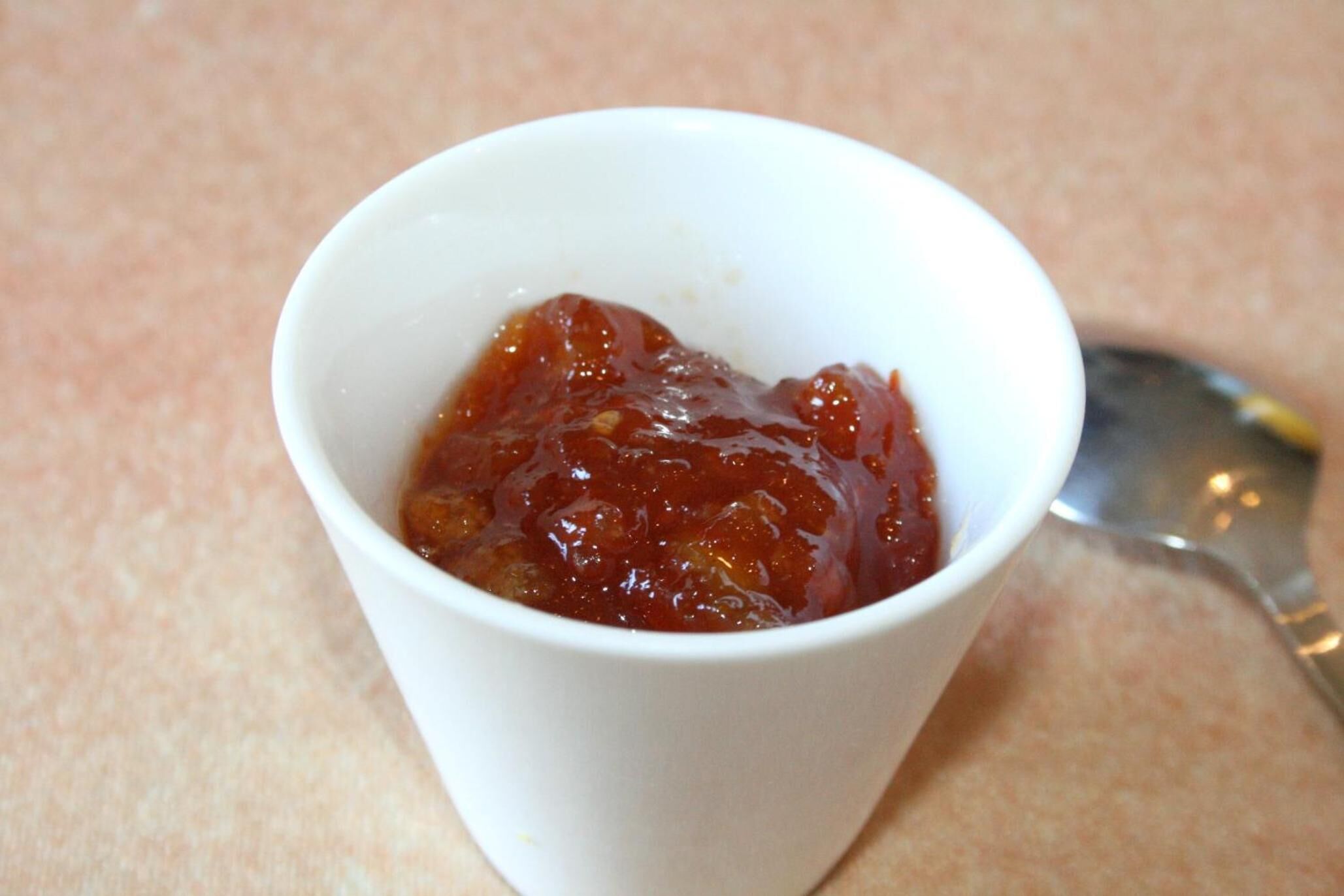 A white cup containing a red substance, possibly jam or jelly, on a textured surface.