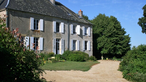 A two-story stone house with white shutters, a gravel driveway, and lush greenery. - Chambres d'hotes du Jay (La Guerche-sur-l'Aubois)