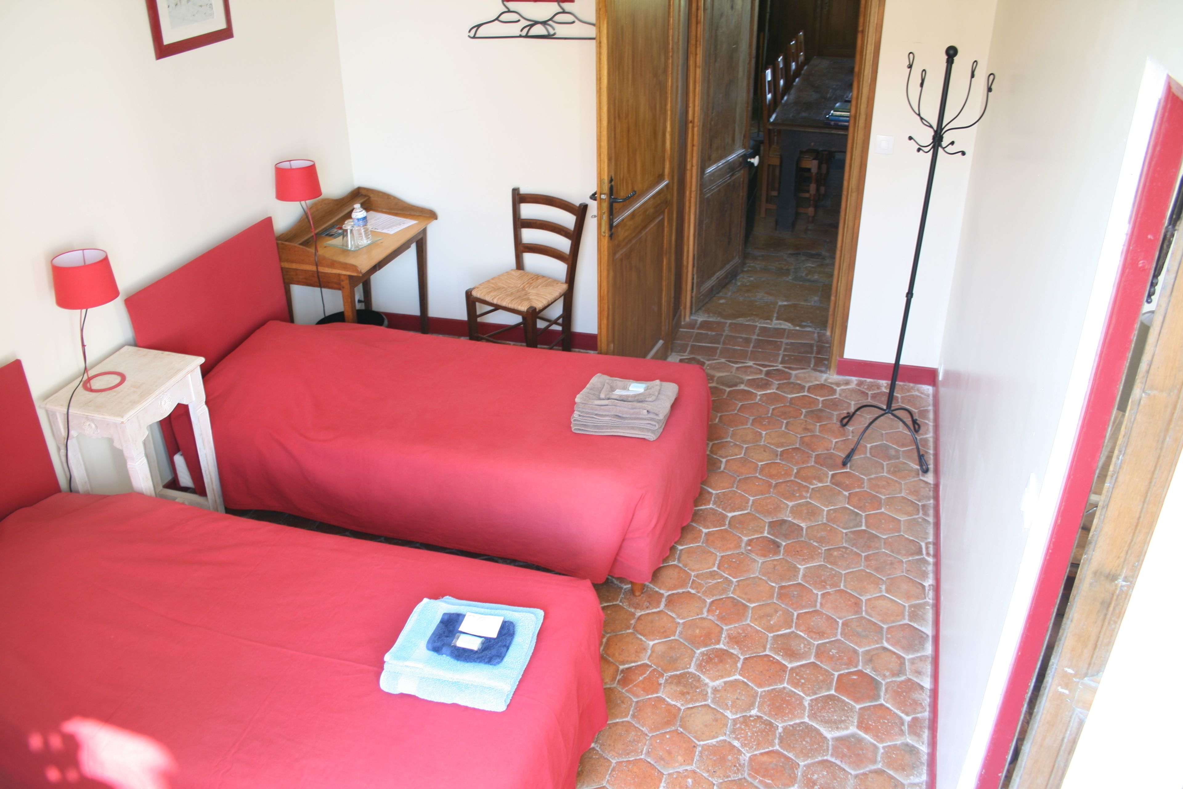 Una habitación con dos camas individuales, una mesita con una silla, una lámpara y un perchero.