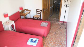 Una habitación con dos camas individuales, una mesita con una silla, una lámpara y un perchero.