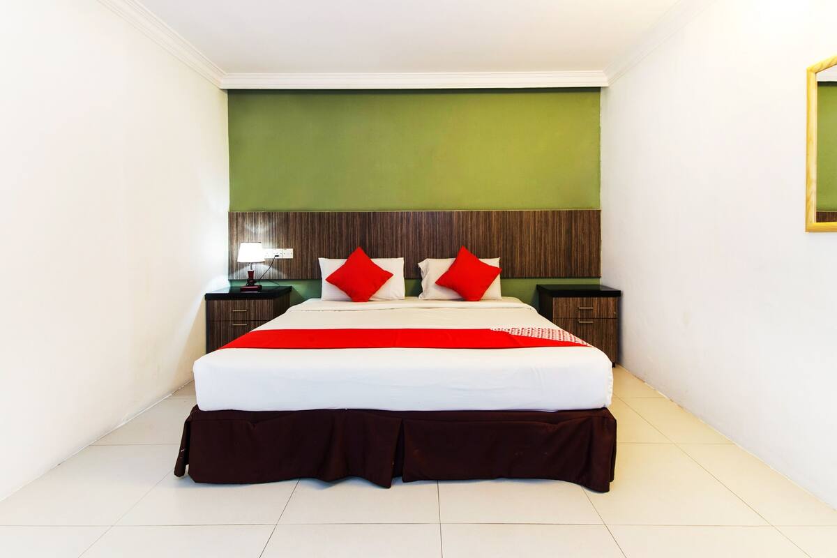 Habitación de hotel con una cama grande, pared verde decorativa, cabecera de madera, dos mesitas de noche con lámparas y un espejo en la pared.