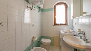 A bathroom with white tiles, a toilet, a sink, and a window. - Villa Agave (Trinità d'Agultu e Vignola)