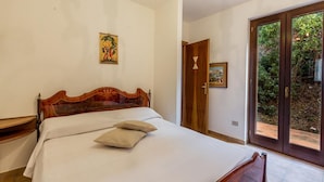 A bedroom with a wooden bed, a nightstand, a door with a glass panel, and a painting on the wall. - Villa Agave (Trinità d'Agultu e Vignola)