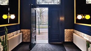 Een donkerblauwe gang met een deur naar buiten, een radiator en een marmeren vloer.