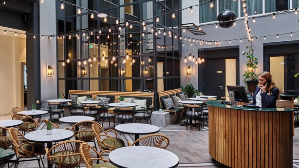 Een modern caféruimte met ronde tafels, rieten stoelen en een houten receptiebalie.