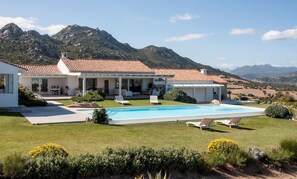 Une maison avec une piscine, un patio doté de chaises longues et un paysage montagneux en toile de fond.