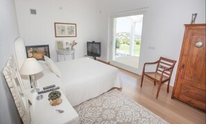 Une chambre à coucher comprenant un lit, une chaise, un téléviseur, une armoire et une fenêtre donnant sur l’extérieur.