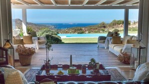 Un espace extérieur aménagé, abrité et doté de sièges, offrant une vue sur une piscine et la mer.